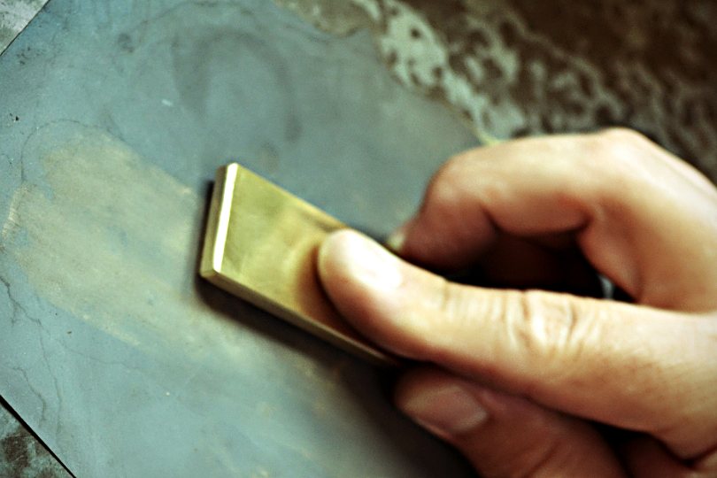 Hand führt einen Messingstempel über eine Werkbank